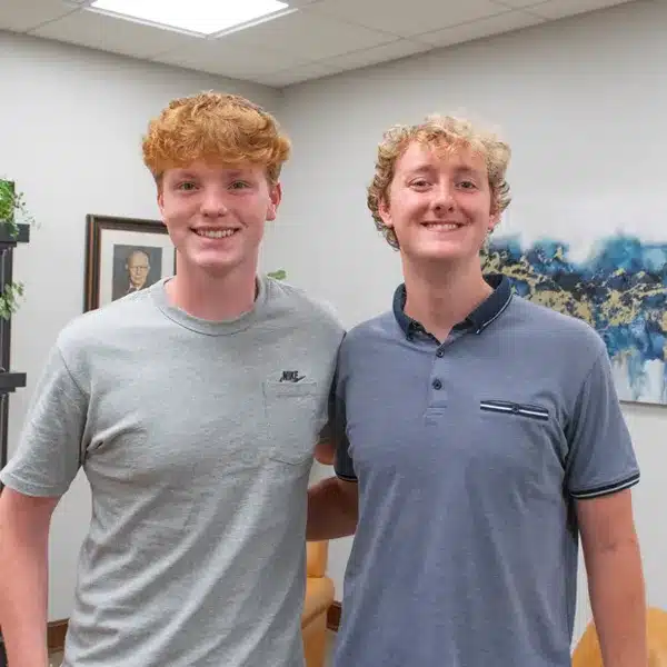 2025-lensing-scholarship-recipients-600w two college-age males standing inside office lobby smiling