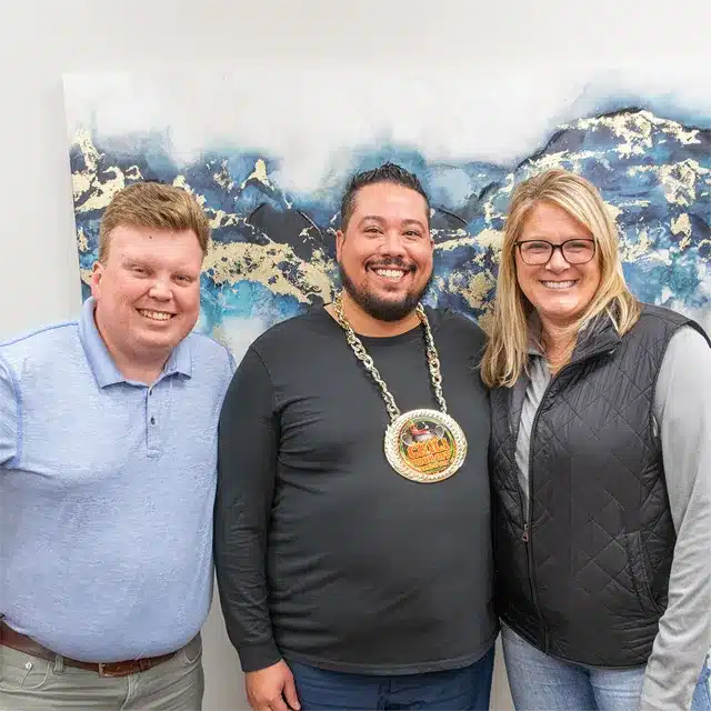 three young adults posing for photo with the center adult wearing a large gold chain