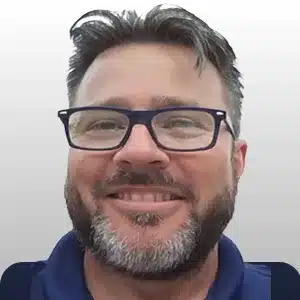 eric-johnson adult male with black framed glasses, black hair and black and gray facial hair wearing a blue shirt