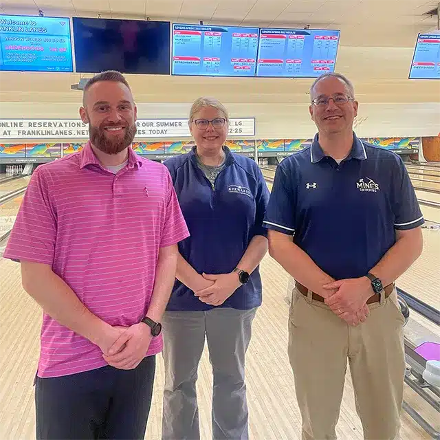 three adults posing for photo inside bowling alley