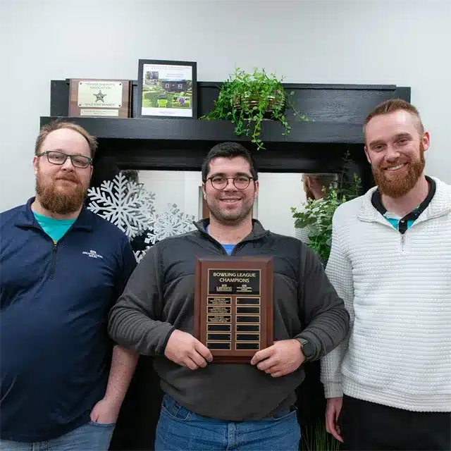 three adult men smiling while holding bowling trophy