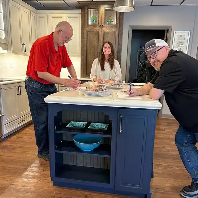 three adults huddled around a kitchen island signing books